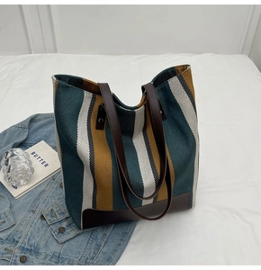 Detail of colorful striped canvas tote bag with brown leather handles on white bedsheet
