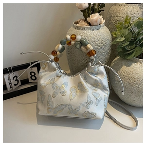 Détail d'un sac blanc en jacquard papillon avec poignée en perles et cordon de serrage argenté