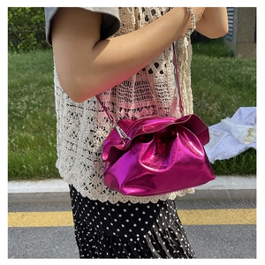 Detail of rose red metallic pleated cloud bag showing texture and drape on a model