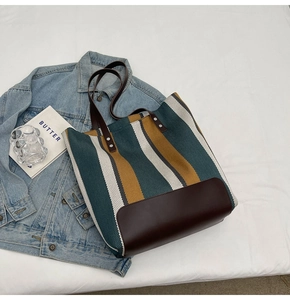 Detailed flat lay of striped canvas tote bag with brown leather handles and denim jacket