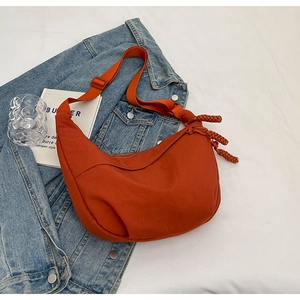 Vue détaillée du sac bandoulière en nylon orange avec sangle nouée sur tissu blanc