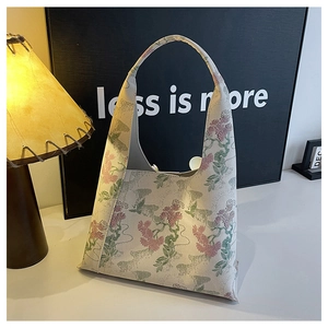 Close-up of floral embroidery on a cream shoulder bucket bag in a warm indoor setting