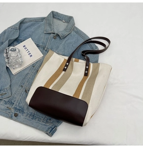 Detail of canvas tote bag with brown stripes and leather handles on blue denim fabric