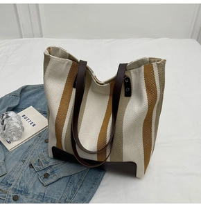 Detail of canvas tote bag with brown leather handles and striped texture on white bedding