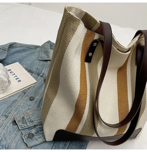 Detailed view of the striped canvas tote bag with brown leather handles on white bedding