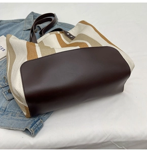 Detail of striped canvas tote with brown leather base and dual shoulder straps