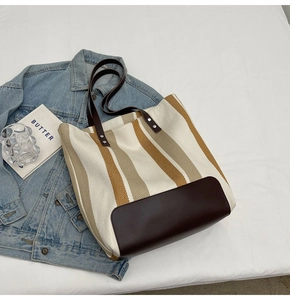 Detail of striped canvas tote bag with brown faux leather handles and rivet accents