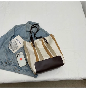 Detail of canvas tote bag with brown stripes and leather base on a soft white bed