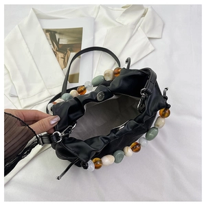 Détail du sac plissé noir avec de grandes perles colorées sur la poignée main