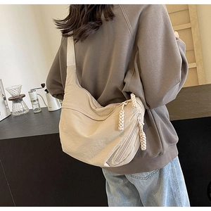 Détail du sac croissant en nylon beige avec tirette tressée porté par un mannequin au café