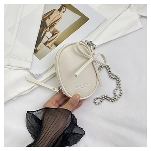 Primer plano de mini bolso de cuero beige con lazo y cadena plateada fina
