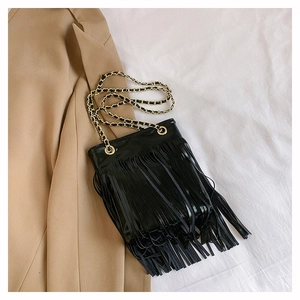Détail du sac à bandoulière noir à franges avec chaîne dorée sur tissu blanc