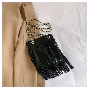 Détail du sac à bandoulière à franges noires avec chaîne dorée sur fond de blazer