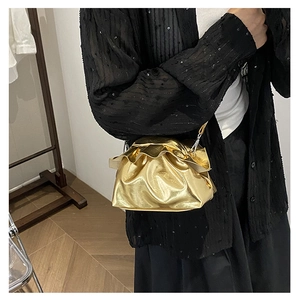 Detail of a metallic gold pleated cloud bag with magnetic closure and slim shoulder strap