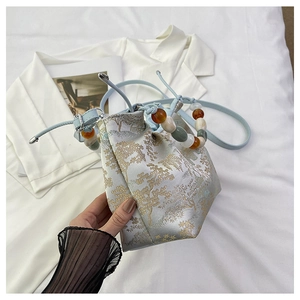 Détail du sac seau en brocart bleu avec motifs dorés et poignée en perles colorées