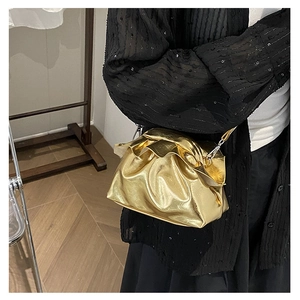 Detail view of a metallic gold pleated cloud bag with a silver chain strap on a model