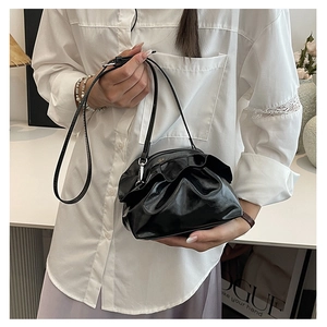 Close-up of black ruched cloud bag with leather strap and metal clasp on white shirt