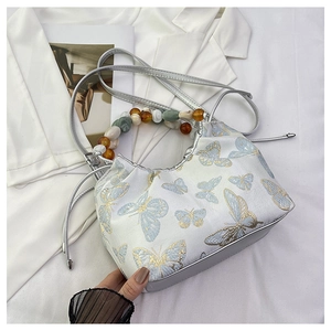 Détail du sac en soie avec broderie papillon bleu et poignée en perles colorées