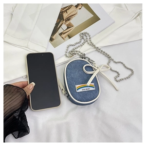 Detalle de mini bolso denim con lazo blanco y parche de arcoíris junto a un teléfono móvil