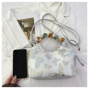 Détail de la broderie papillon et de la poignée en perles sur un sac en soie blanche
