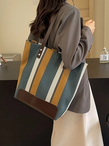 Large striped canvas tote bag with brown leather handles worn by a model in casual style