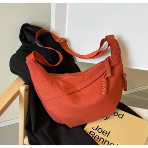 Détail d'un sac demi-lune en nylon orange avec fermeture éclair sur une chaise en bois