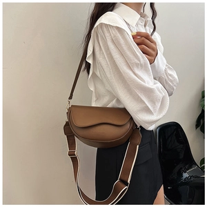 Brown leather saddle bag with broad woven shoulder strap worn as a crossbody bag by a model