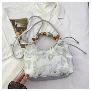 Broderie détaillée de papillons bleu clair et dorés sur un sac à main blanc perle