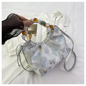 Détail d'un sac en satin avec broderie papillon bleue et poignée en perles vintage
