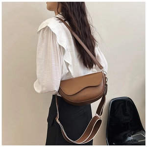Detail of dark brown saddle bag with wavy flap and dual stylish shoulder straps