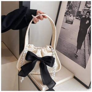 Detail of off-white corduroy bag with large black bow and drawstring closure