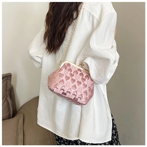 Pink heart-embossed evening bag with gold chain strap worn by a model in casual attire