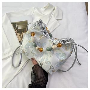 Détail de la broderie papillon et de la poignée en perles sur un sac en soie
