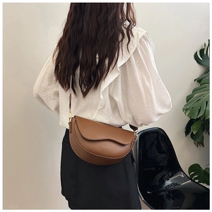 Detail showing the brown saddle bag with wavy flap design and textured synthetic leather