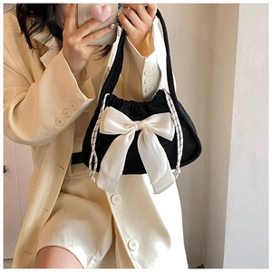 Detailed view of black knitted bag featuring a large white satin bow and drawstring closure