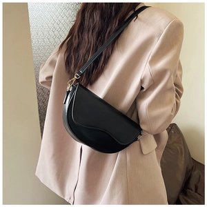 Detail view of a matte black saddle bag featuring an irregular flap and gold hardware