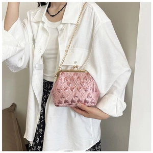 Pink heart-embossed evening bag with gold chain strap worn cross-body by a model