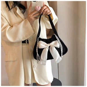 Detail of black corduroy handbag with a large white bow and drawstring side texture