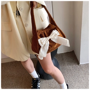 Detail of brown corduroy handbag featuring a large white satin bow on model's outfit