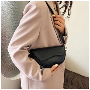 Detail of black saddle bag with wavy flap design and gold hardware on a model