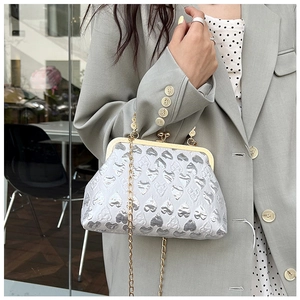 Detail of silver heart-embossed evening bag with golden clasp and delicate chain strap