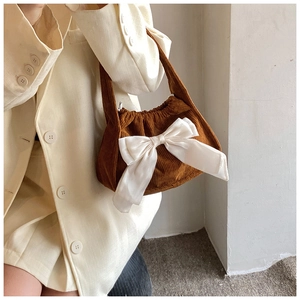 Detail of brown corduroy handbag with a large white satin bow on a beige blazer background