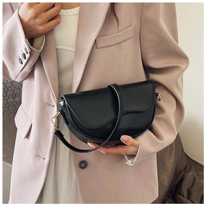 Macro detail of black saddle handbag with gold buckle held by a model in a beige blazer
