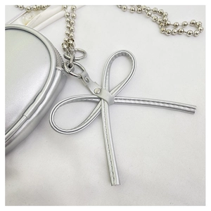 Detalle del mini bolso de corazón plateado con colgante de lazo y cadena de bolas