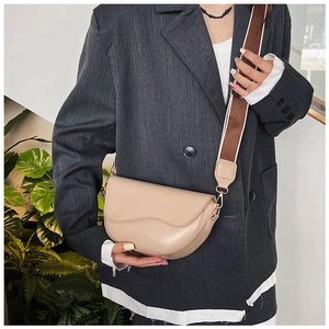 Detail view of the beige saddle bag featuring wavy stitching and a wide fabric strap