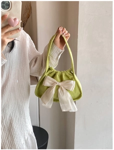 Detail of light green ruched handbag with a large cream bow worn by a model