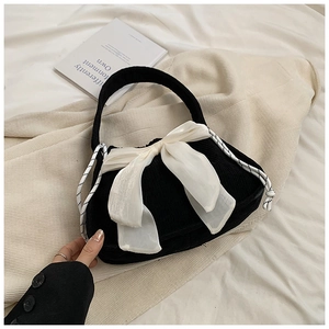 Detail view of black corduroy handbag with a large white silk bow and woven rope decoration