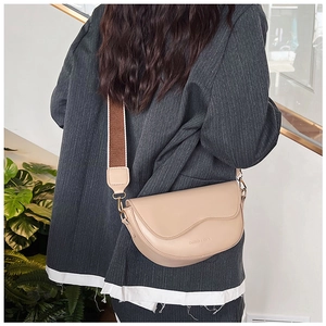 Close-up of beige saddle bag featuring a wavy edge cover and striped wide strap