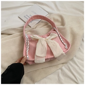 Close-up of pink corduroy handbag featuring a large cream satin bow and woven drawstring