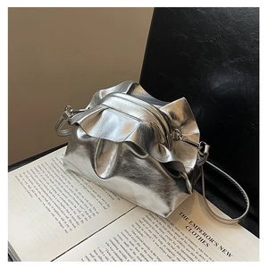 Detailed view of silver metallic pleated shoulder bag resting on an open book over leather chair